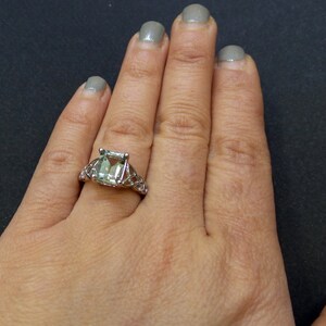 May include: A silver ring with a large, emerald-cut green gemstone set in a delicate, intricate design.