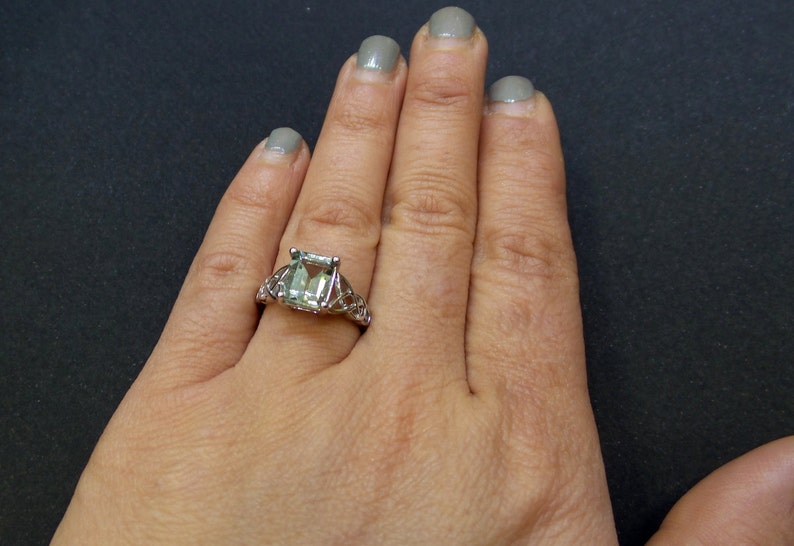 May include: A silver ring with a large, emerald-cut green gemstone set in a delicate, intricate design.