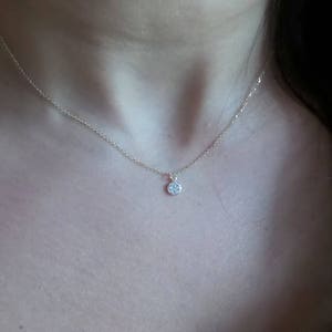 Op de afbeelding: Een delicate gouden ketting met een klein, rond hangertje bezet met kleine glinsterende steentjes.