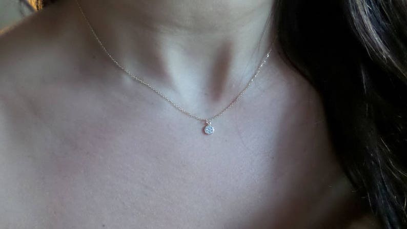 Op de afbeelding: Een delicate gouden ketting met een klein, rond hangertje bezet met kleine glinsterende steentjes.