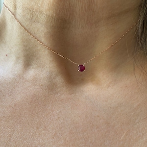 Può includere: Una delicata collana a catena d'oro con un ciondolo di pietra rossa.