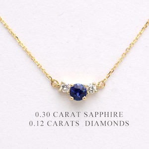 May include: A delicate gold necklace featuring a central, round, deep blue sapphire gemstone, flanked by two smaller, sparkling diamonds. The necklace is a fine jewelry piece, with the text "0.30 CARAT SAPPHIRE" and "0.12 CARATS DIAMONDS" below.