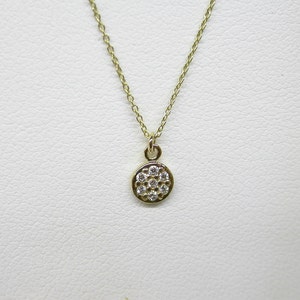 Op de afbeelding: Een delicate gouden ketting met een klein rond hangertje bezet met glinsterende witte diamanten.