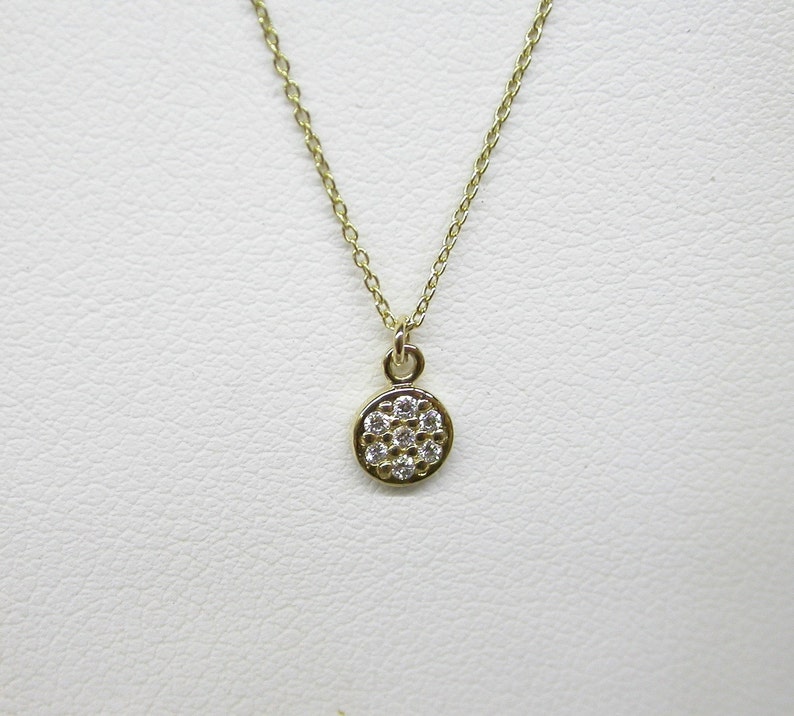 Op de afbeelding: Een delicate gouden ketting met een klein rond hangertje bezet met glinsterende witte diamanten.