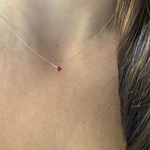 May include: A delicate rose gold necklace with a single, small ruby gemstone pendant.