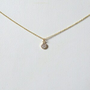 Op de afbeelding: Een delicate gouden ketting met een klein rond hangertje bezet met kleine glinsterende diamanten.