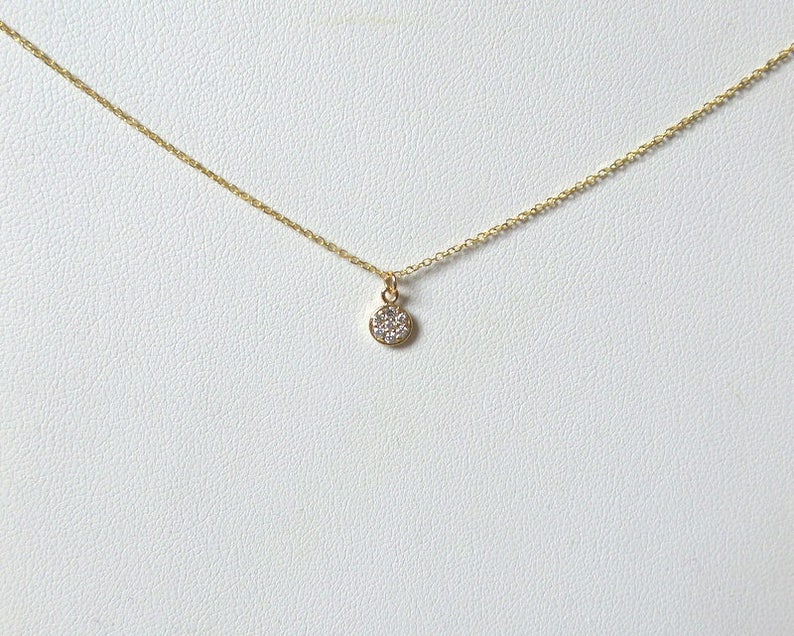 Op de afbeelding: Een delicate gouden ketting met een klein rond hangertje bezet met kleine glinsterende diamanten.