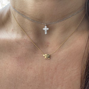 May include: A woman wearing two necklaces. The top necklace is a silver chain with a diamond cross pendant. The bottom necklace is a gold chain with a bear pendant.