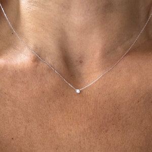 May include: A delicate silver chain necklace with a small, clear diamond pendant.