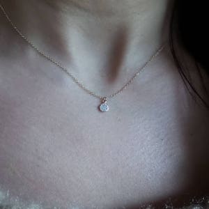 Op de afbeelding: Een delicate zilveren ketting met een klein, rond hangertje met een enkele, heldere edelsteen.