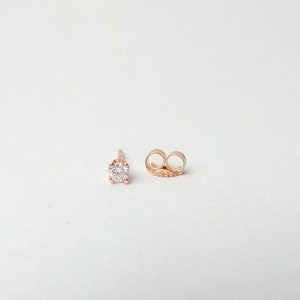 May include: A single rose gold stud earring with a small, clear round diamond.