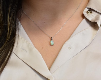 Puede incluir: Un collar de cadena de plata con un delicado colgante de ópalo ovalado. El ópalo es de color verde claro con destellos de arcoíris.