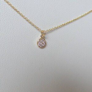 Op de afbeelding: Een delicate gouden ketting met een klein, rond hangertje dat is bezet met kleine witte diamanten.