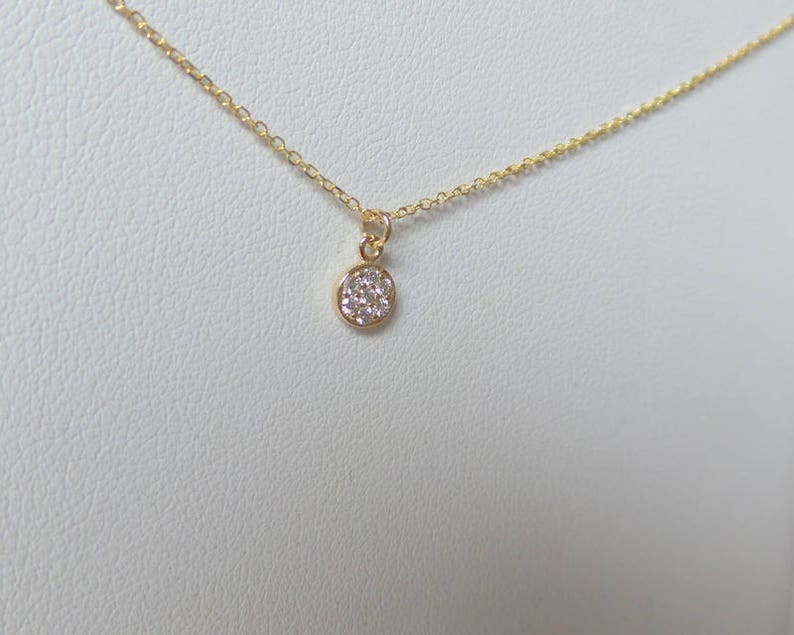 Op de afbeelding: Een delicate gouden ketting met een klein, rond hangertje dat is bezet met kleine witte diamanten.