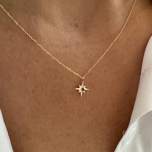 Puede incluir: Un collar de cadena dorada con un colgante de estrella con una pequeña piedra preciosa roja en el centro.