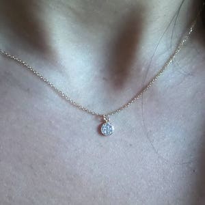 Op de afbeelding: Een delicate gouden ketting met een klein, rond hangertje bezet met kleine glinsterende steentjes.