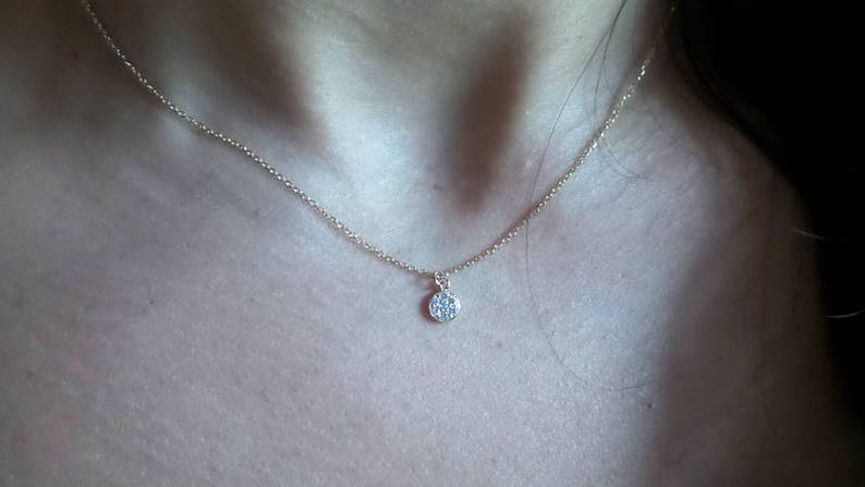 Op de afbeelding: Een delicate gouden ketting met een klein, rond hangertje bezet met kleine glinsterende steentjes.