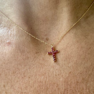May include: A gold chain necklace with a small red gemstone cross pendant.