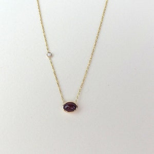 May include: A gold chain necklace with a small, oval-shaped, dark purple gemstone pendant and a single, small, clear diamond accent.