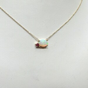 May include: A delicate gold chain necklace with a white opal pendant accented by two small red gemstones.