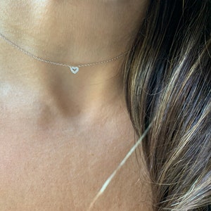 Pode incluir: Um delicado colar de corrente de prata com um pequeno pingente de coração cravejado de diamantes.