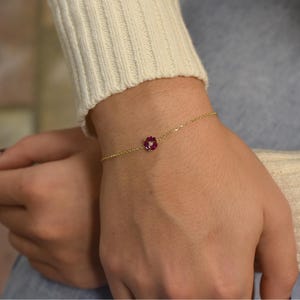 Può includere: Un delicato braccialetto a catena dorata con un'unica pietra rossa.
