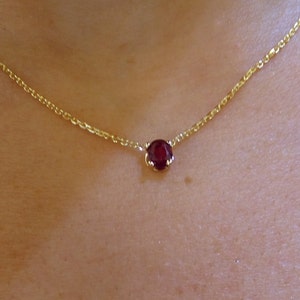 Puede incluir: Un delicado collar de cadena de oro con un solo colgante de piedra roja oscura redonda.