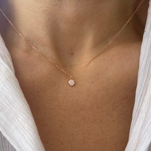May include: A delicate rose gold necklace with a small, round pendant encrusted with tiny white stones.