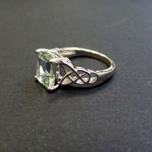 May include: A silver ring with a green emerald-cut gemstone set in a Celtic knot design.