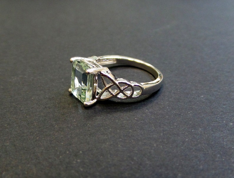May include: A silver ring with a green emerald-cut gemstone set in a Celtic knot design.
