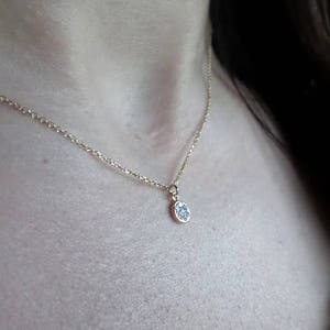 Op de afbeelding: Een delicate gouden ketting met een klein, rond hangertje bezet met kleine glinsterende steentjes.