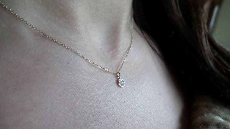 Op de afbeelding: Een delicate gouden ketting met een klein, rond hangertje bezet met kleine glinsterende steentjes.
