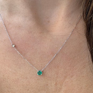May include: A silver chain necklace with a small emerald green gemstone pendant and a smaller clear gemstone pendant.
