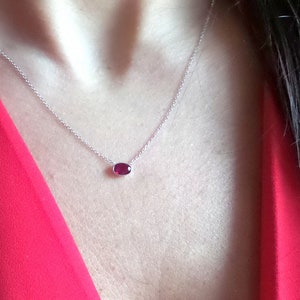 Op de afbeelding: Een delicate zilveren ketting met een klein ovaalvormig robijn hanger.