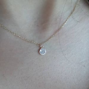 Op de afbeelding: Een delicate gouden ketting met een klein, rond hangertje dat is bezet met kleine, glinsterende steentjes.