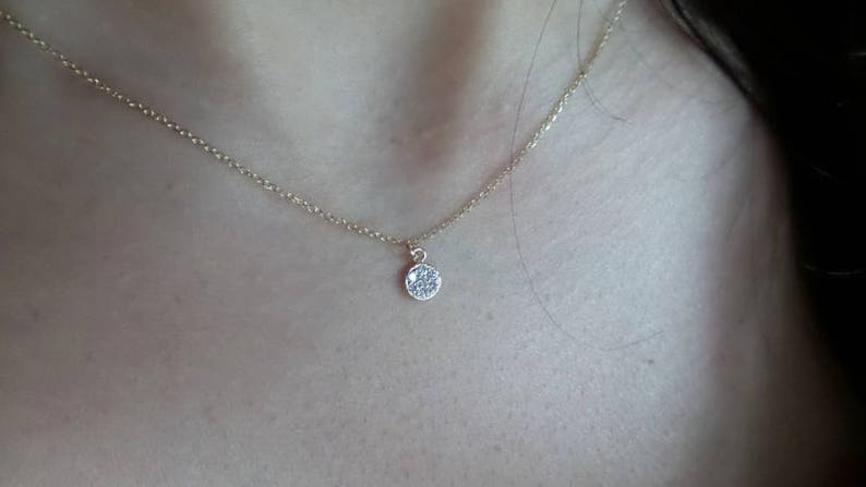 Op de afbeelding: Een delicate gouden ketting met een klein, rond hangertje dat is bezet met kleine, glinsterende steentjes.