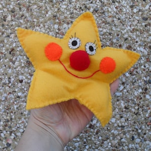 May include: A yellow felt star with a smiling face, red nose, and orange cheeks. The star is handmade and has a stitched outline.