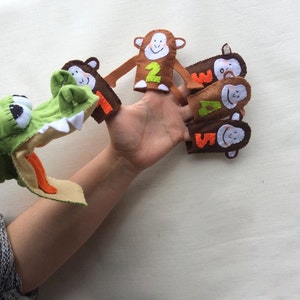 May include: A green crocodile puppet with an open mouth and a set of five brown finger puppets with monkey faces and numbers 1 through 5.
