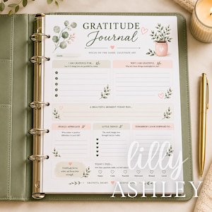May include: A gratitude journal page inside a sage green binder with a gold ring mechanism. The page features the text Gratitude Journal, sections for daily reflections, lists for things to be grateful for, and small illustrations of plants.
