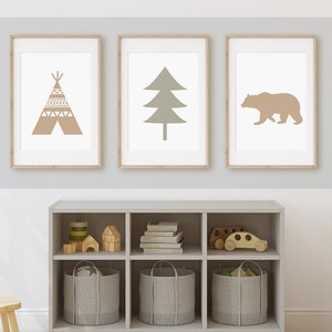 May include: Three framed prints on a light gray wall. The prints feature a brown teepee, a green tree, and a brown bear. A gray wooden shelf with six cubbies is below the prints. The cubbies contain wooden toys, books, and gray woven baskets.