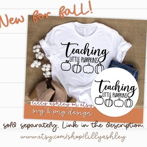 May include: White t-shirt with black text that reads "Teaching Little Pumpkins" and a row of four pumpkins. The shirt is on a brown surface with a pair of brown boots and a white circle with the same text and pumpkins.
