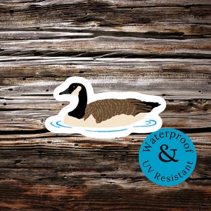 May include: A sticker of a brown and white goose swimming in blue water. The sticker is on a wooden background and has a blue circle with the text "Waterproof & UV Resistant" on it.