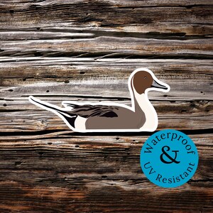 May include: A brown and white duck with a long, thin bill. The duck is swimming on a wooden surface. The duck is a sticker with a blue circle that says "Waterproof & UV Resistant".