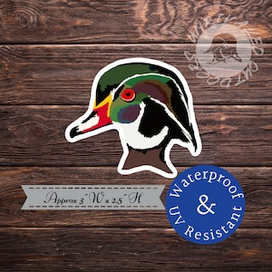 May include: A colorful sticker of a wood duck head with a white outline. The sticker is approximately 3 inches wide by 2.5 inches high. The sticker is waterproof and UV resistant.