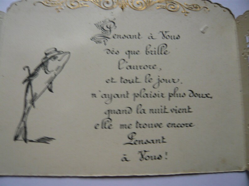 K&ouml;nnte beinhalten: Eine Vintage-Karte mit einer Schwarzwei&szlig;illustration eines Fisches, der einen Hut tr&auml;gt und einen Stock h&auml;lt. Die Karte hat einen goldenen Rand und enth&auml;lt ein handgeschriebenes Gedicht auf Franz&ouml;sisch, das lautet: "Pensant &agrave; Vous d&egrave;s que brille l'aurore, et tout le jour. n'ayant plaisir plus doux, quand la nuit vient elle me trouve encore Pensant &agrave; Vous!"