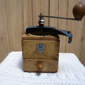 May include: A vintage wooden coffee grinder with a blue metal top and a drawer. The grinder has a lion logo with the text "Lion Brand" on the front.