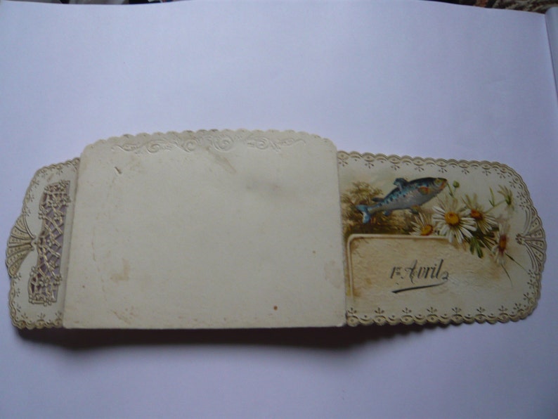 K&ouml;nnte beinhalten: Eine vintage, wei&szlig;e Karte mit Spitzenrand, einer Illustration eines blauen und wei&szlig;en Fisches und dem Text "5 Avril" auf der rechten Seite.