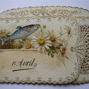 K&ouml;nnte beinhalten: Eine vintage Karte in Cremefarbe mit einem goldenen Rand und einem zarten Spitzenmuster. Die Karte zeigt ein gemaltes Bild eines Fisches, der &uuml;ber einem Strau&szlig; wei&szlig;er G&auml;nsebl&uuml;mchen schwimmt. Der Text "1er Avril" ist in schwarzer Tinte auf die Karte geschrieben.