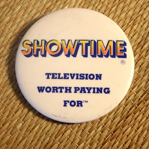 May include: A white round button with the text "SHOWTIME" in blue and orange letters. Below the text is "TELEVISION WORTH PAYING FOR" in blue letters.