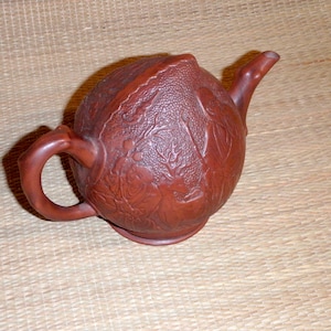 May include: A brown ceramic teapot with a rounded body and a carved design of a deer and trees. The teapot has a spout and a handle.